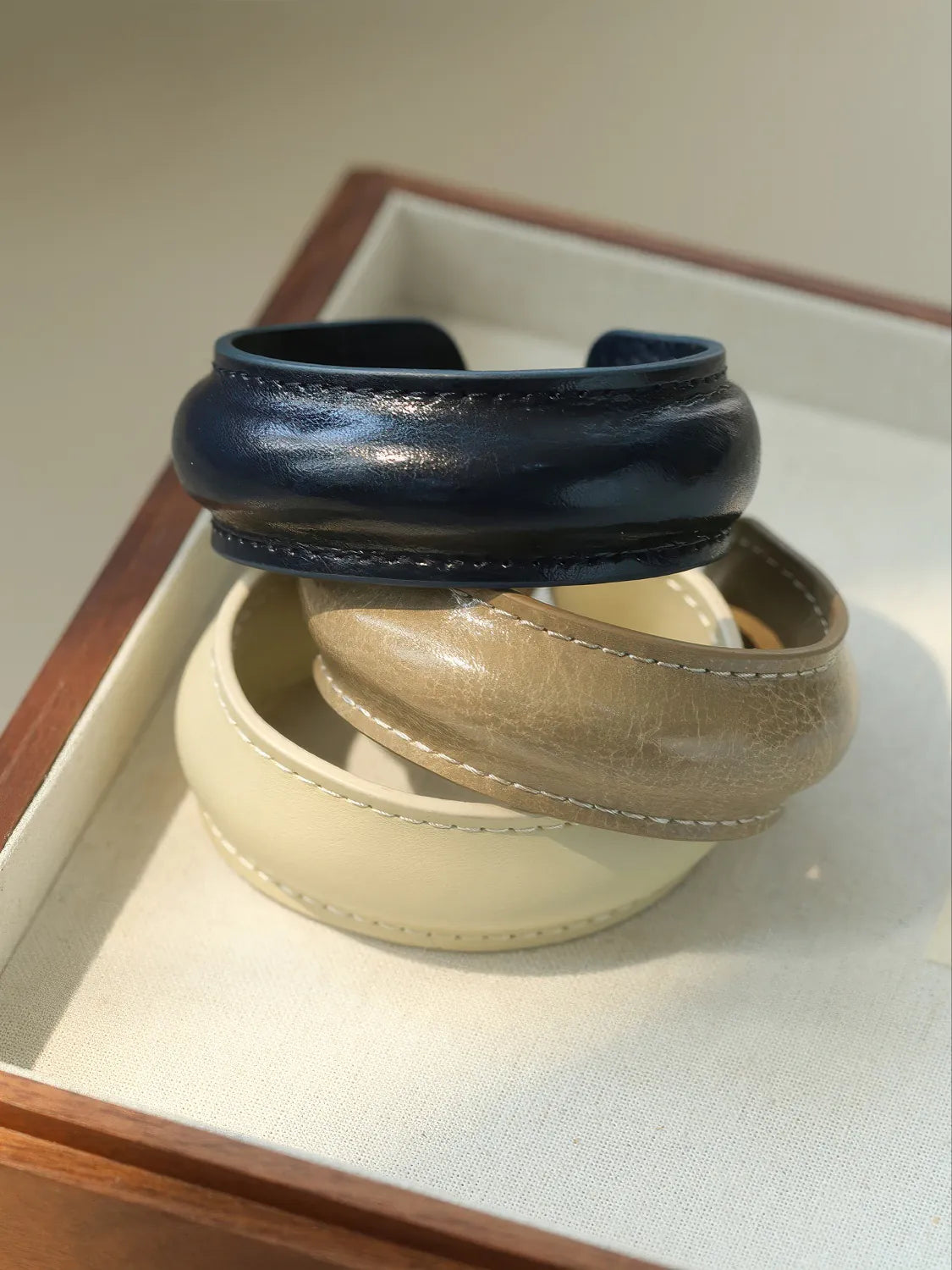 Two leather bracelets, one navy and one beige, on a light surface.
