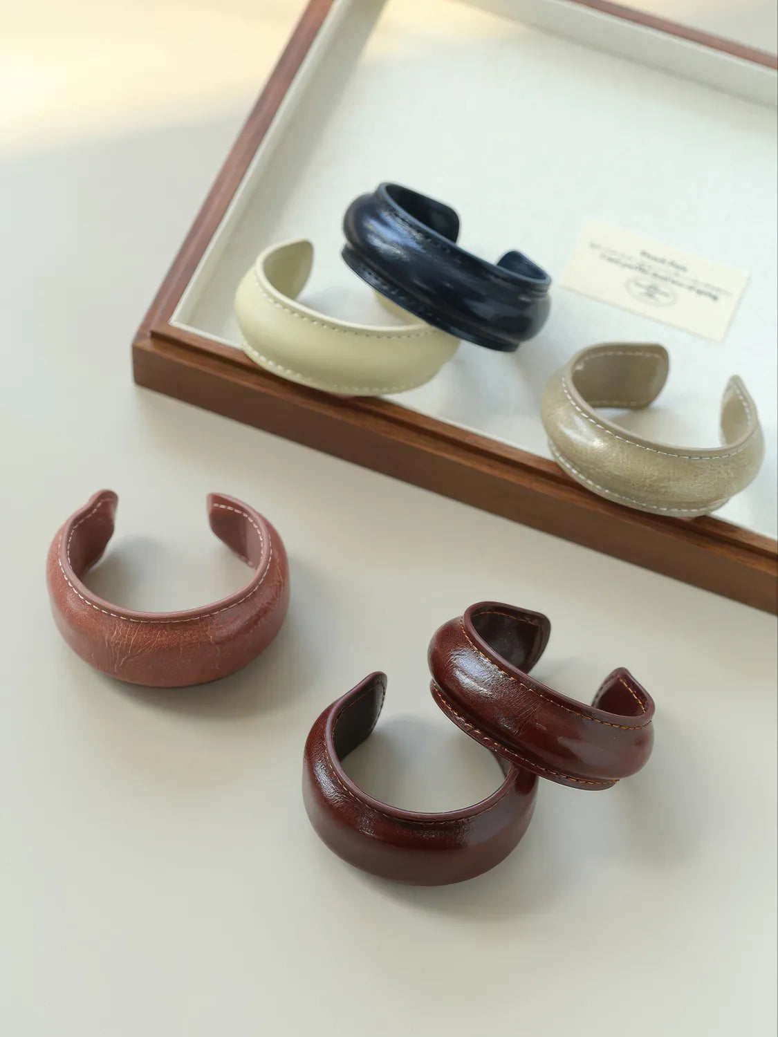 Set of leather bracelets in various colors displayed on a wooden tray.