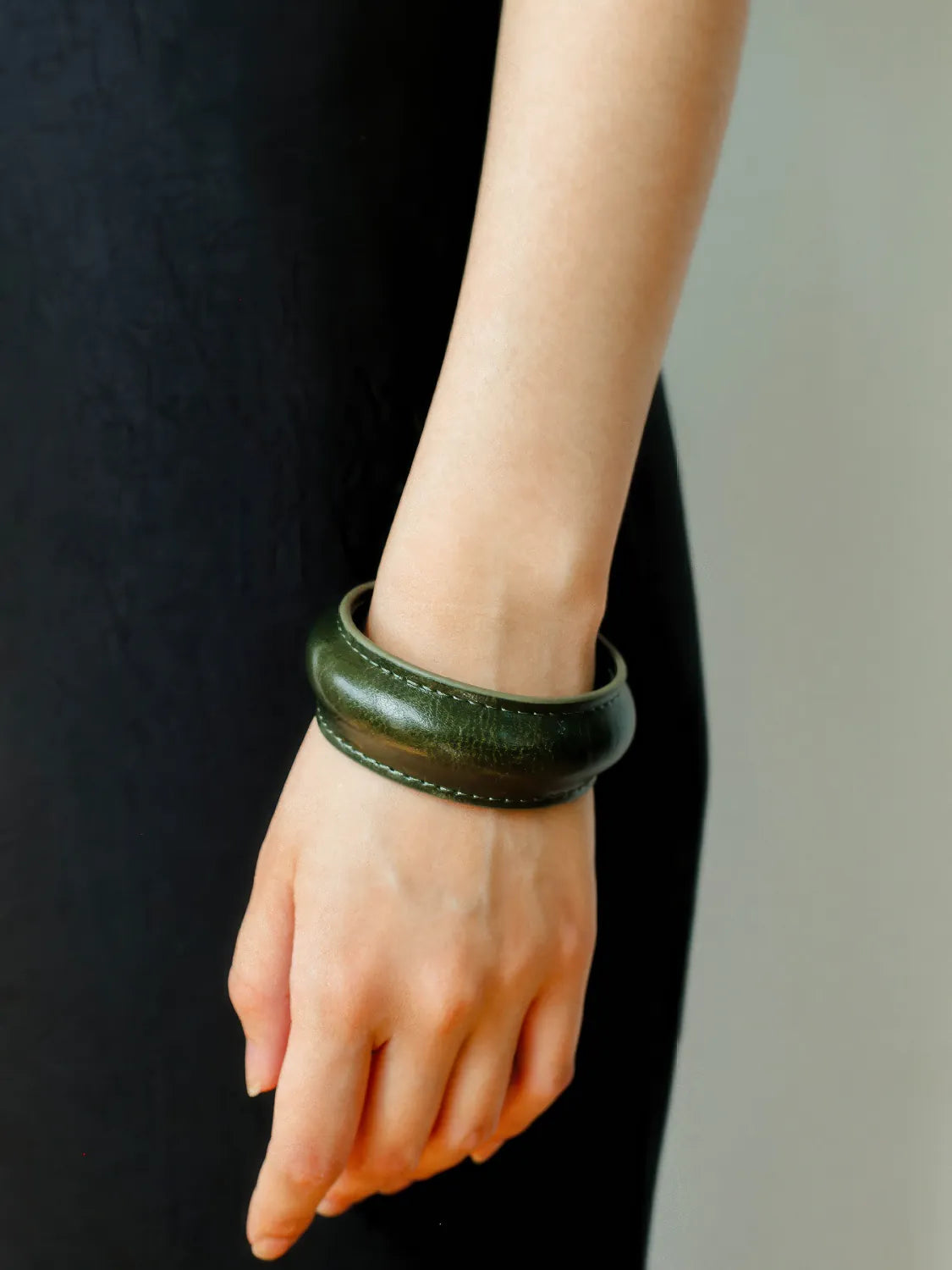 Hand wearing a green leather bracelet against a black background