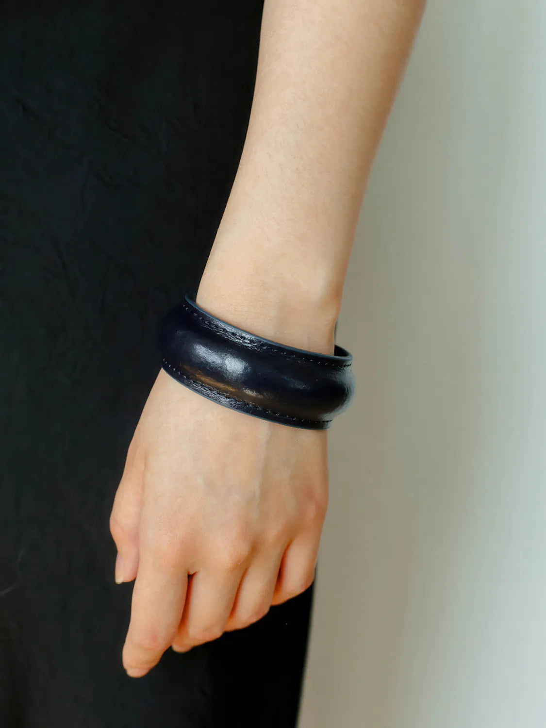 Black leather bracelet on a wrist against a neutral background